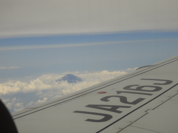 飛行機の窓からまだ雪の残る富士山の頂を見る